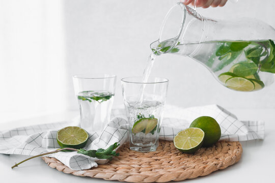Detox water with lime fruit. Hand pouring lime fruit water from jug into glasses