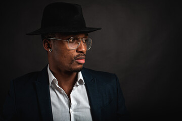 Fototapeta na wymiar Portrait of attractive, handsome, pretty, serious and stylish professional african american businessman executive with stylish suit and white shirt and black hat isolated on dark background. Low key. 