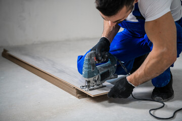 Builder in blue work clothes sawing laminate boards with an electric saw