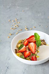 Homemade crunchy granola with nuts, dried fruits, fresh strawberries, mint and yogurt (fermented baked milk) on a white plate. Healthy breakfast concept.