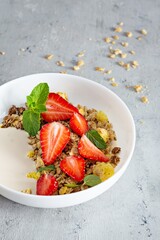 Homemade crunchy granola with nuts, dried fruits, fresh strawberries, mint and yogurt (fermented baked milk) on a white plate. Healthy breakfast concept.