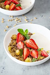 Homemade crunchy granola with nuts, dried fruits, fresh strawberries, mint and yogurt (fermented baked milk) on a white plate. Healthy breakfast concept.