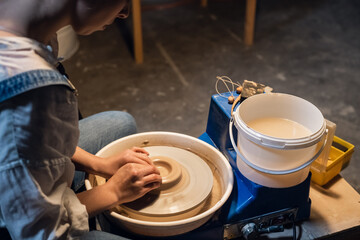 master class on sculpting a pot in an art workshop. the girl behind the potter's wheel makes a blank with her hands