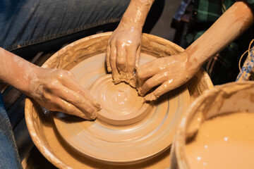 teacher and student sculpt a pot of clay on a potter's wheel, close-up