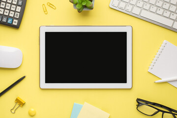 Photo overhead of notebook keyboard calculator pen tablet computer mouse notes plant glasses and paperclips isolated on the yellow background