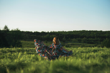 girl in a blue dress whirl in a green field of rye in the rays of the setting sun