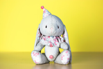 A cute Easter bunny toy with a funny cap on yellow background. Happy Easter minimalism concept. A postcard for Easter. A gray hare soft toy on yellow background. Place for text with congratulations.