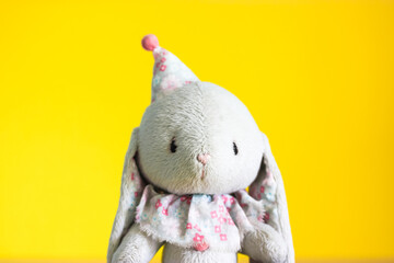 A cute Easter bunny toy with a funny cap on yellow background. Happy Easter minimalism concept. A postcard for Easter. A gray hare soft toy on yellow background. Place for text with congratulations.