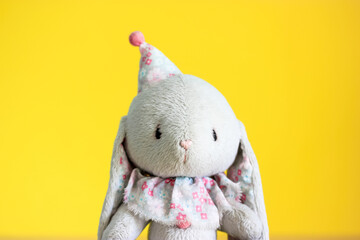 A cute Easter bunny toy with a funny cap on yellow background. Happy Easter minimalism concept. A postcard for Easter. A gray hare soft toy on yellow background. Place for text with congratulations.
