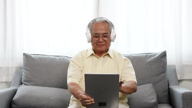 Happy Senior male using laptop computer listening enjoy music song in online streaming digital technology wifi internet connection, Elderly retired life at home concept.