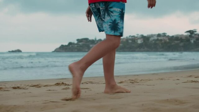 Unrecognizable boy spending summer at seaside. Unknown man walking at seashore.