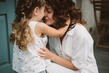 Portrait of little daughter kissing her beautiful happy mother
