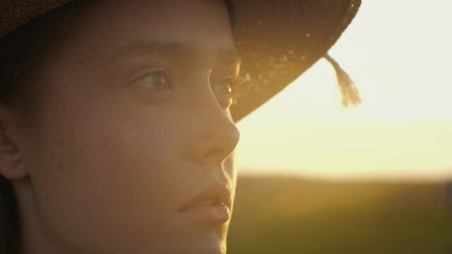 Close Up Portrait of Beautiful Young Woman is opening her Eyes while standing outside on a fresh Air. Blonde Girl Enjoying freedom, Nature in Countryside. Wearing a Straw Hat. Summer Evening, Sunset.