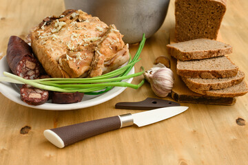 baked meat and blood sausage on a plate, green onion and garlic on wooden background, home cooking