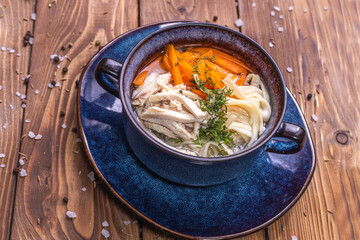 A cup of soup with chicken meat, pasta, carrots, seasoned with fresh herbs.