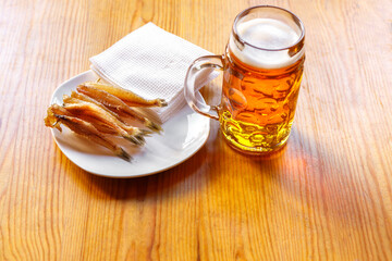 A mug of beer and dried fish strung on a wooden skewer.