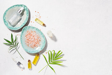 Natural skin care serums, Essential oils and cosmetic sea salt with fresh palm leaves on white marble background long banner format. Organic spa products. 