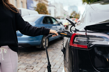 Woman near electric car. Vehicle charged at the charging station.
