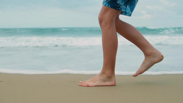 Unrecognizable boy legs going at beach. Unknown guy ejoying summer at seaside.