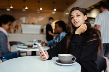 Female student using smartphone while sitting in cafe
