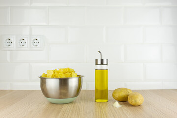 Closeup of a stainless steel bowl with french fries inside next to an oil pan and raw potatoes with salt