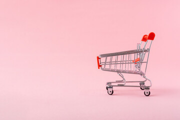 Shopping trolley on light pink background with a copy space.