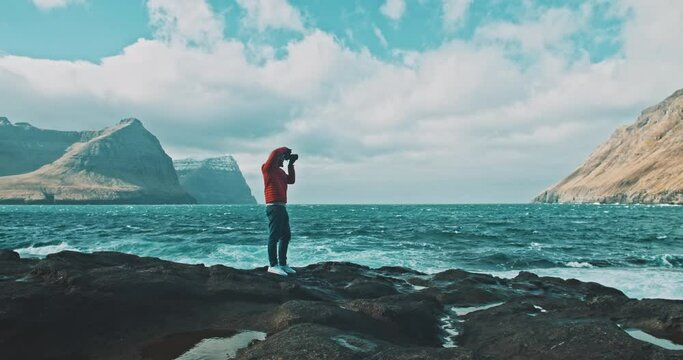 Photographer standing on rocks taking photos of a mountain scenery in front of the ocean.  