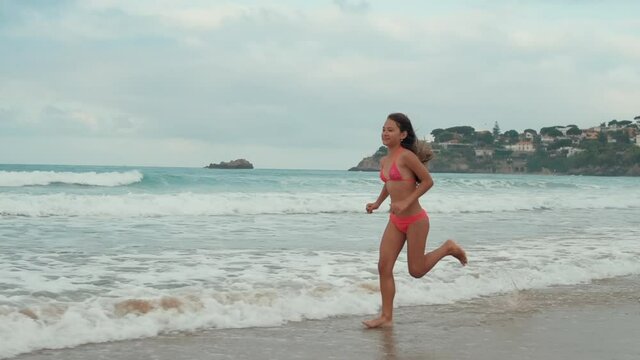 Sporty woman running along coastline in warm day. Athlete girl enjoying sea run