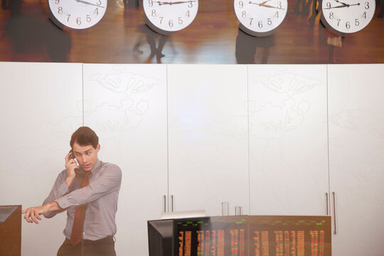 Male stock trader talking on the phone in a trading room with multiple clocks and computer screens