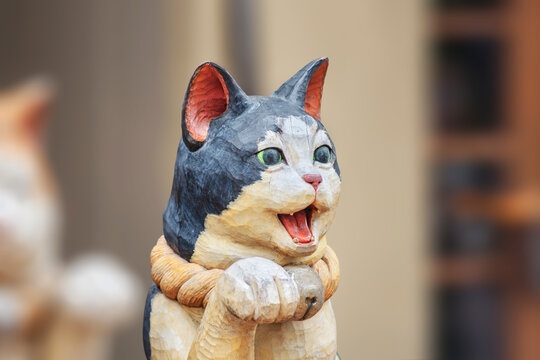 Close up on a wooden sculpture depicting a cute Japanese maneki-neko cat with the mouth open and a paw raised in a beckoning gesture in the Yanaka-Ginza shopping street.