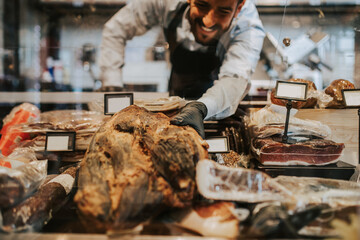 Handsome middle age male seller working at supermarket or grocery store and selling cured meat products and cheeses.