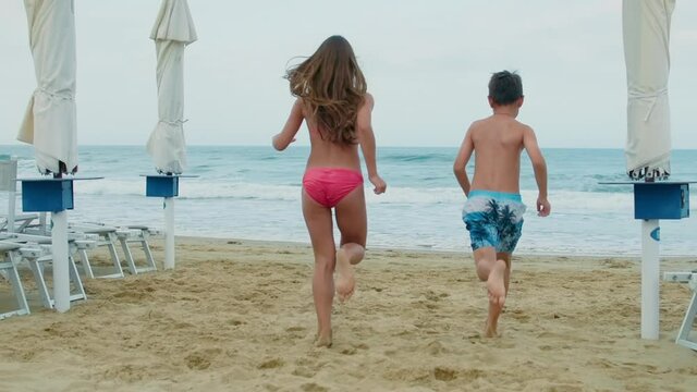 Cheerful children having fun at sand beach. Boy and girl running at seaside.