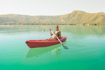 Latin woman paddling in a kayak, she is enjoying her vacation, she is on a red cayak in a turquoise lake and mountains in the background, on a sunny summer afternoon