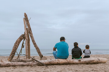 Familia Mexicana compuesta por un padre y sus dos hijos sentados sobre un tronco en una playa de Santa Cruz, California, Estados Unidos.