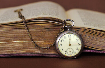 Eine antike Taschenuhr lehnt an einem alten Buch  mit vergilbten Seiten