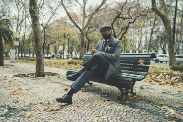 A dapper stately black senior in an elegant custom suit is sitting on a street bench in an autumn...