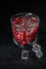 Grains of pomegranate with water and ice cubes on dark background, close up