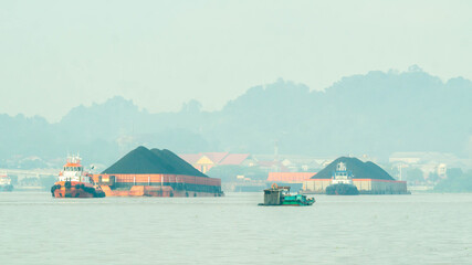 Tugboat drag barge full of coal crossing Mahakam River, Samarinda, in the morning. Transportation and industrial background