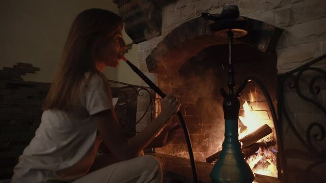Beautiful woman Smoking a hookah sitting by the fireplace