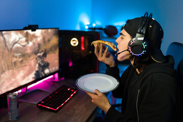 Young gamer eating pizza and gaming on the computer © AntonioDiaz