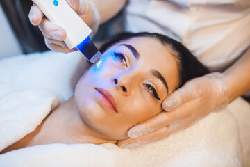 Caucasian brunette woman lying in a spa while having facial treatment procedures with modern technologies