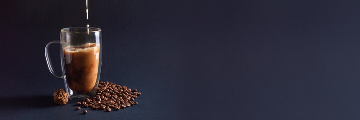 Banner with milk pouring into black coffee in glass cup on dark blue background with beans and chocolate truffle. Coffee love concept. Front view