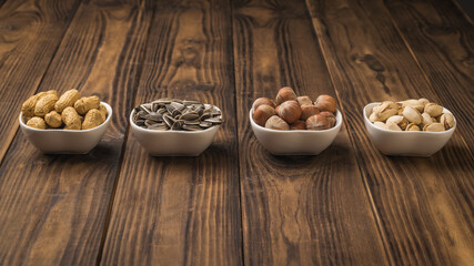 White ceramic bowls with nuts and seeds on a wooden table.