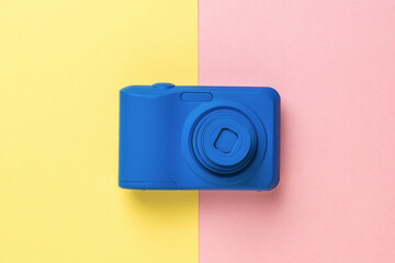 A blue camera on a two-tone yellow and pink background.