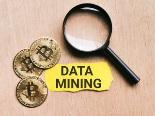 Selective focus phrase Data Mining written on yellow paper strip with golden bitcoin and magnifying glass. Cryptocurrency and finance concept.