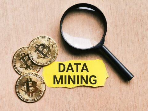 Selective focus phrase Data Mining written on yellow paper strip with golden bitcoin and magnifying glass. Cryptocurrency and finance concept.