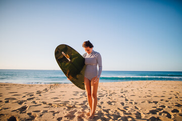 Naklejka na ściany i meble women walking on beach with surfboard