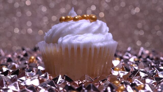 Cute cupcake macro shallow depth of field view. Decoration with sugar sprinkles. Cup cake with white vanilla cream on gold background. Making delicious desserts muffin for birthday or Valentine.