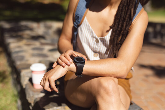 Midsection of african american woman sitting using her smartwatch in park