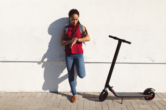 African american woman frowning, checking time on smartwatch scooter next to her